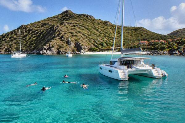 Small sailing catamaran on turquoise water off a green island