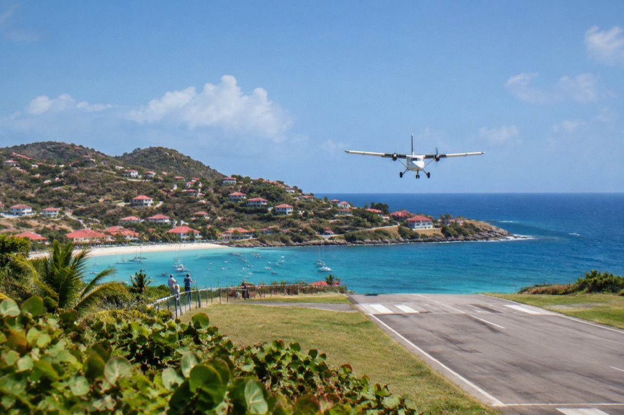 A small turboprop aircraft on a short Caribbean runway between green hills and blue sea