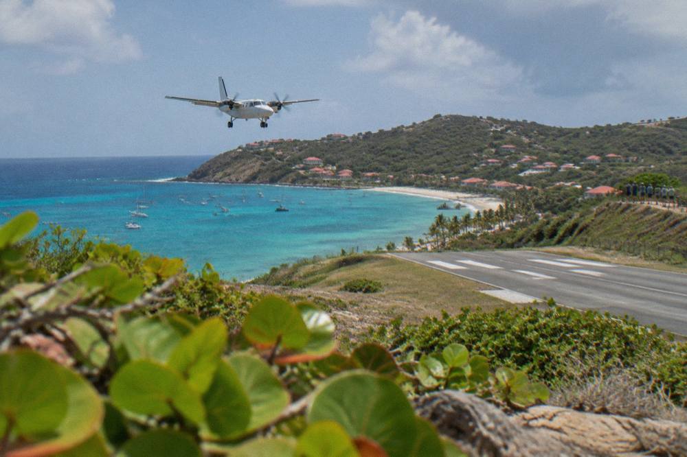 A turboprop descending over turquoise Caribbean water toward a small island airport
