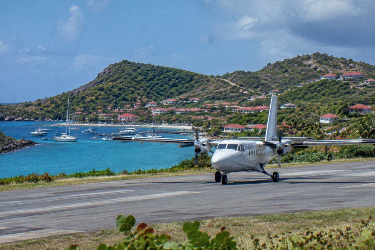 A small turboprop plane on the short runway at Gustavia harbor in St Barts with hills behind it