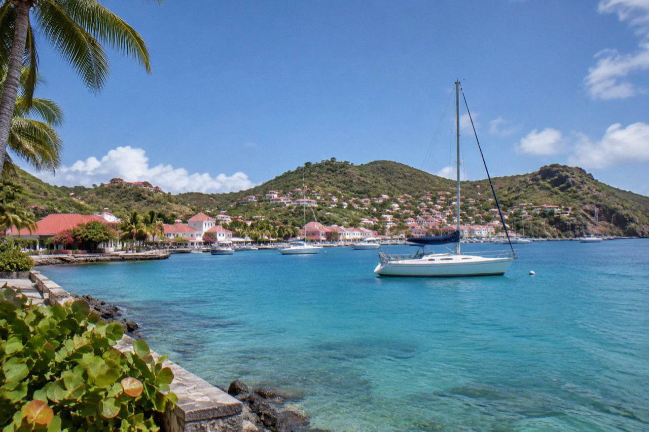 A sailboat anchored in clear turquoise water off a green hillside on St Barts