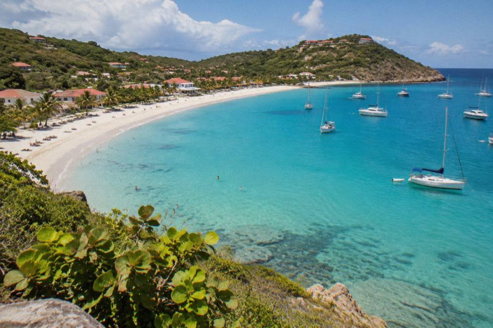 Sailboats anchored in clear water near a green headland in the Caribbean