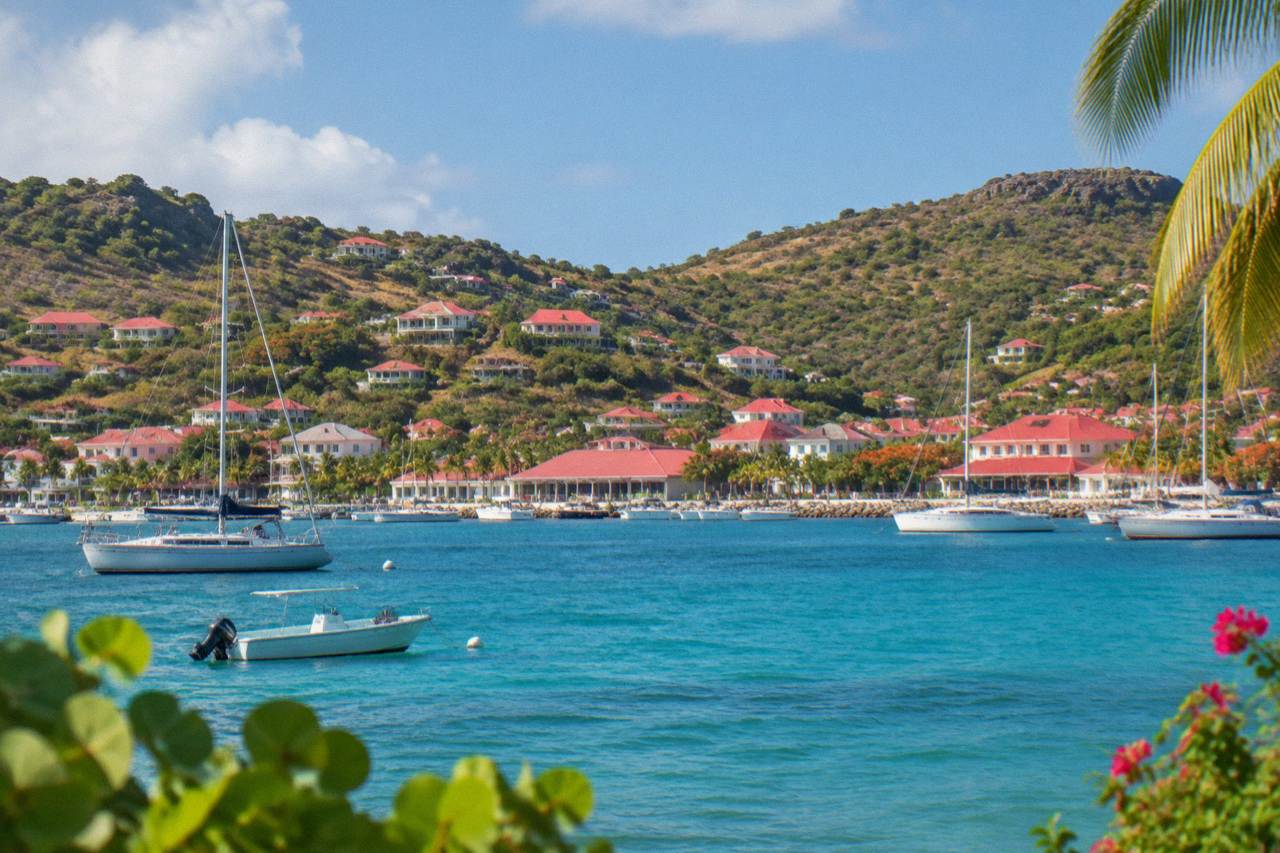 A view across turquoise Caribbean water toward the green hills and red roofs of a small island harbor town