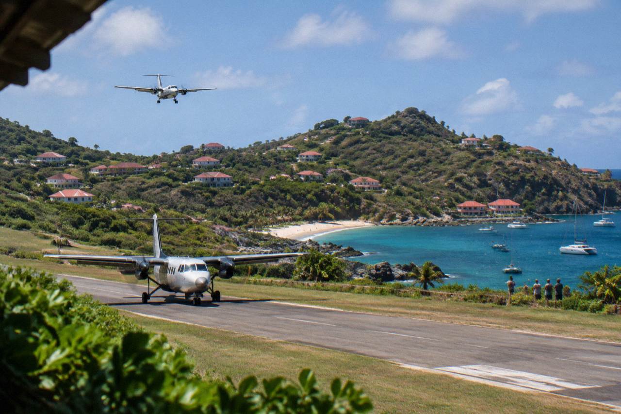 A small turboprop aircraft on the short runway at Gustaf III Airport in St Barts with green hills behind it