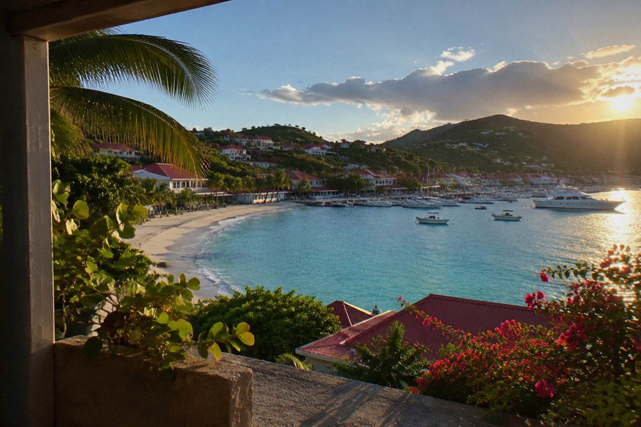 A curved Caribbean beach below green hills with calm turquoise water along the shoreline of St Barts