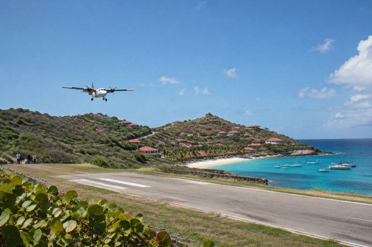A small turboprop aircraft on a short Caribbean runway between green hills and blue water
