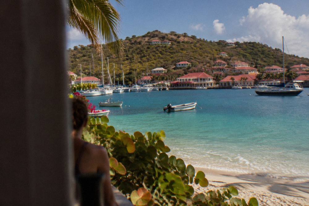 A calm crescent of pale sand and clear shallow water at a beach on St Barts with green hills behind