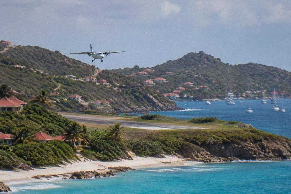A small turboprop airplane on a short runway beside a beach with hills behind it