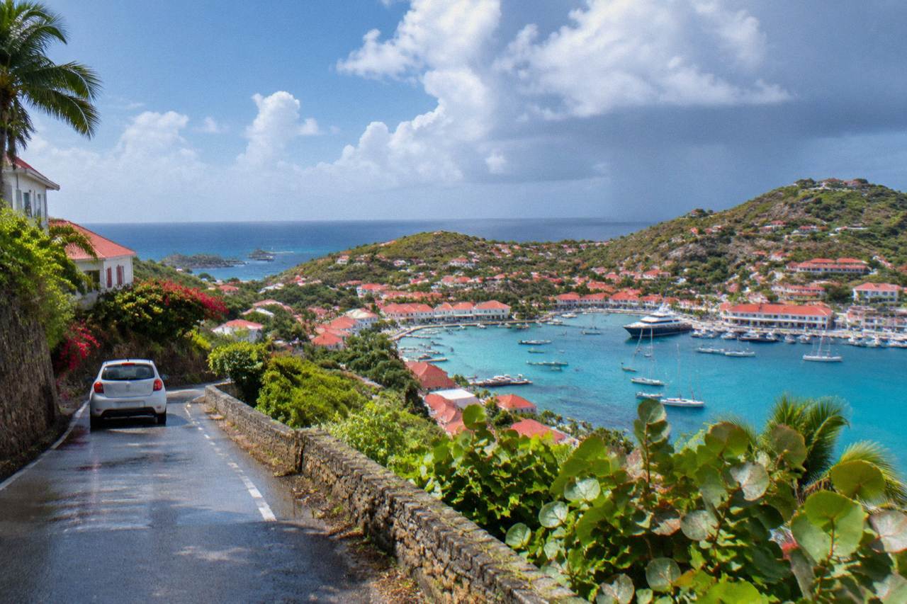 A small rental car on a narrow hillside road above the turquoise coastline of St Barts