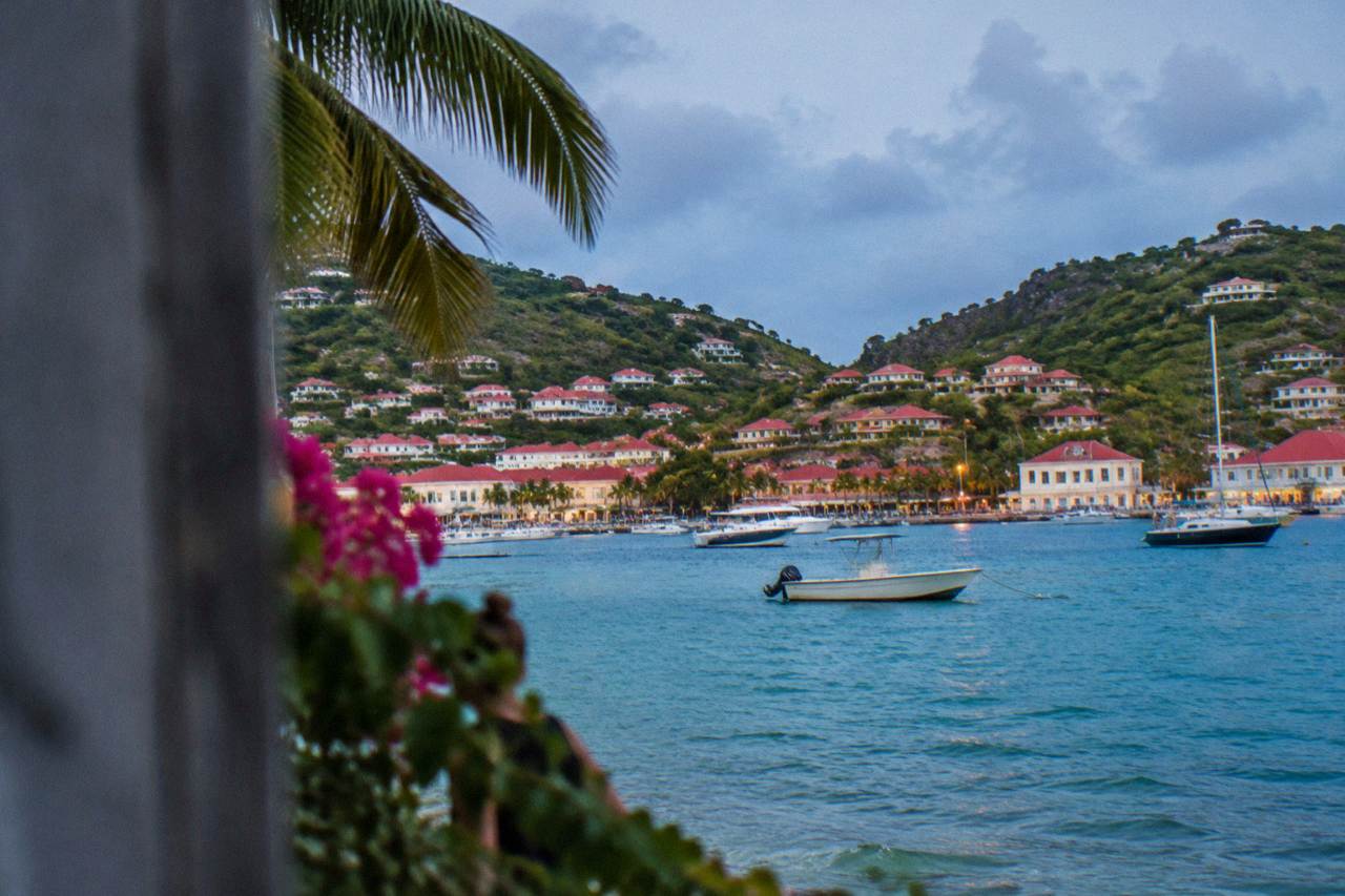 A view across turquoise Caribbean water toward green hills with red roofs on a small island coastline