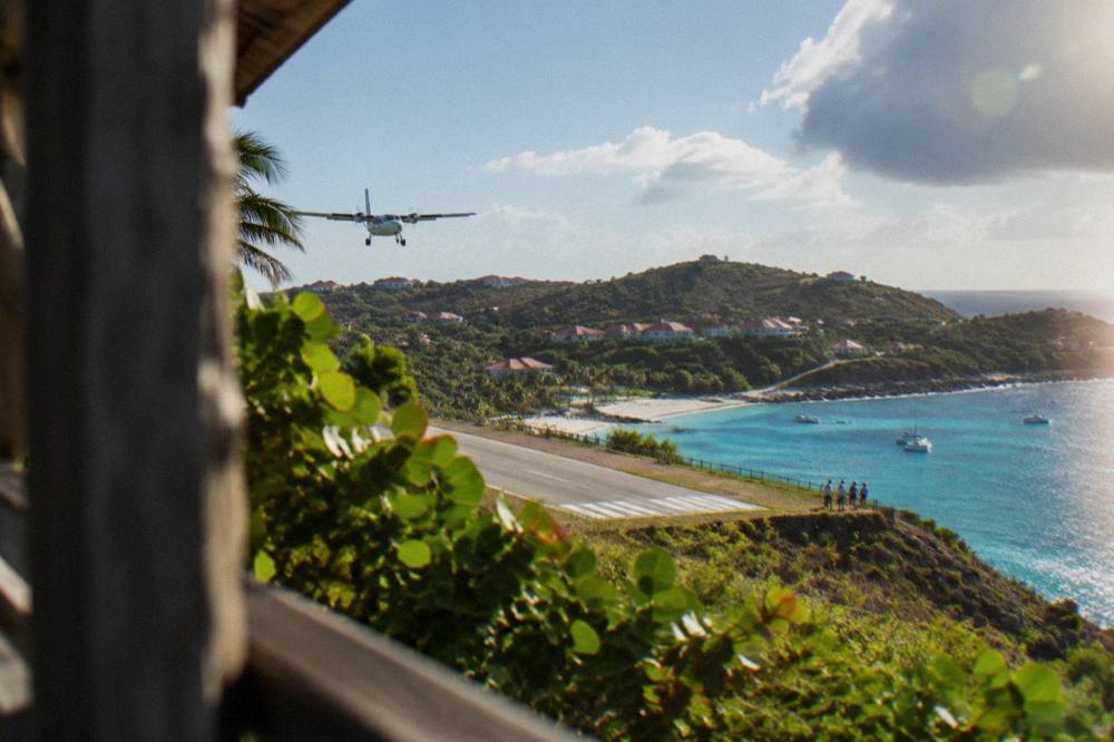A small turboprop aircraft on a short runway between a hillside and a Caribbean beach