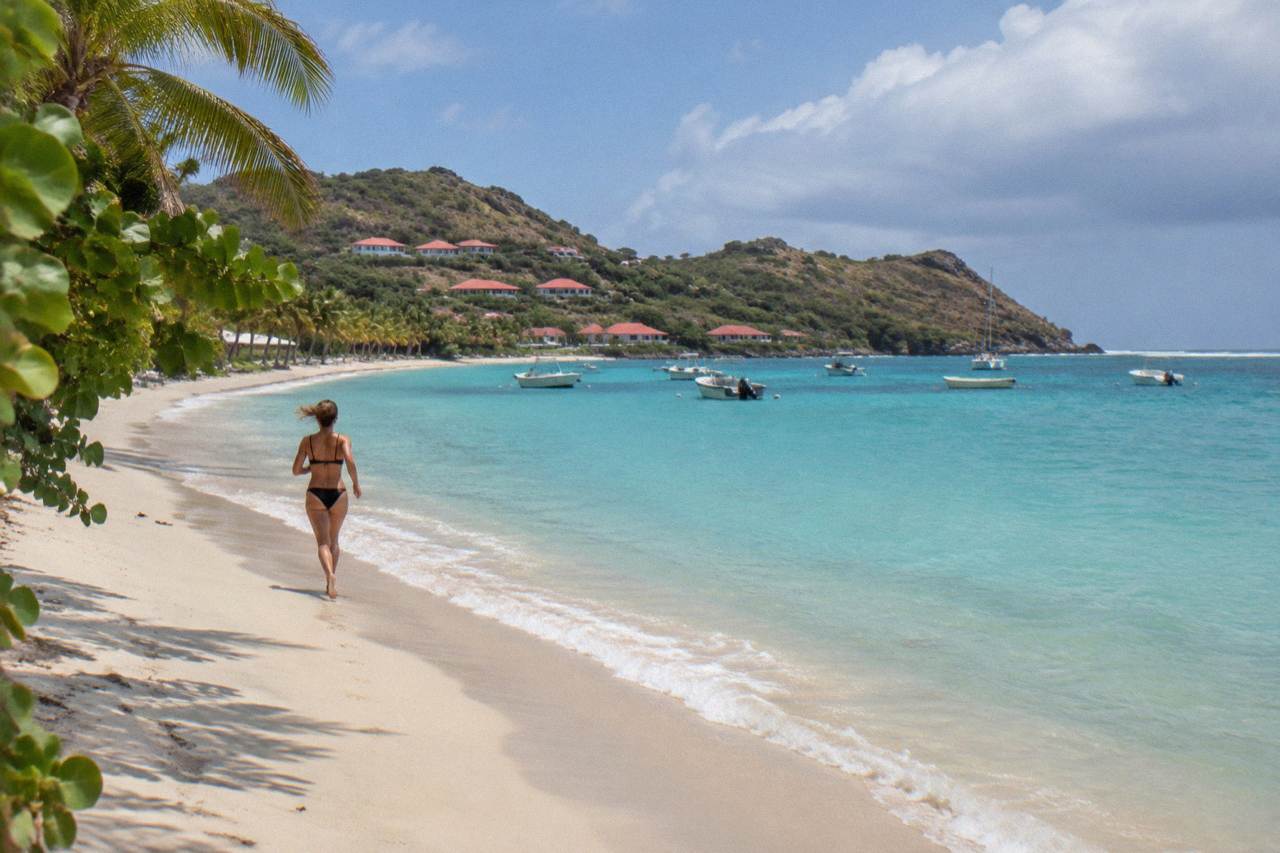 A calm crescent of pale sand and turquoise water on a Caribbean island with green hills behind