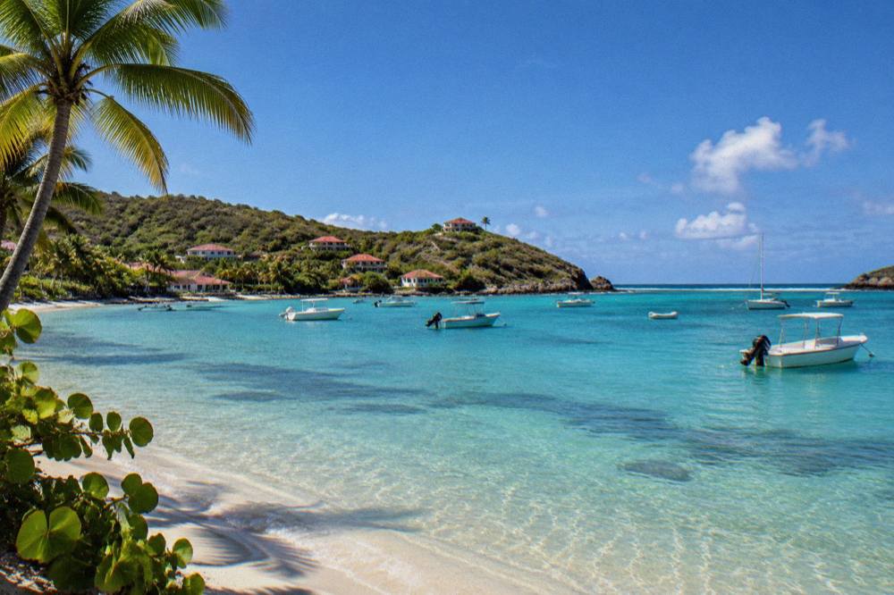 Small boats anchored in clear shallow water beside a green headland at a Caribbean bay