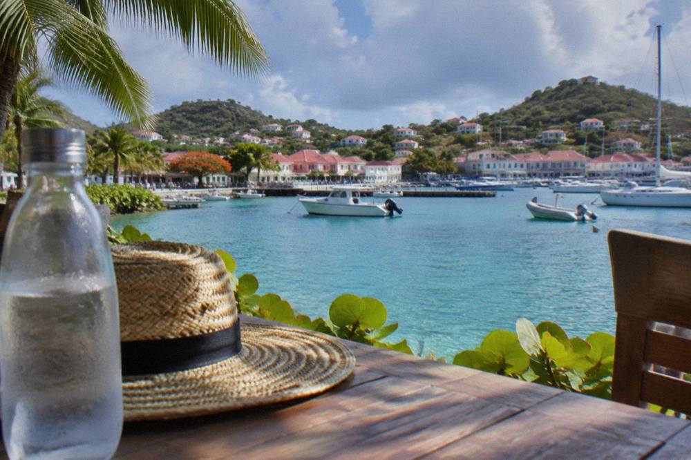 Bottled water and a sun hat on a wooden table beside a view of turquoise Caribbean water