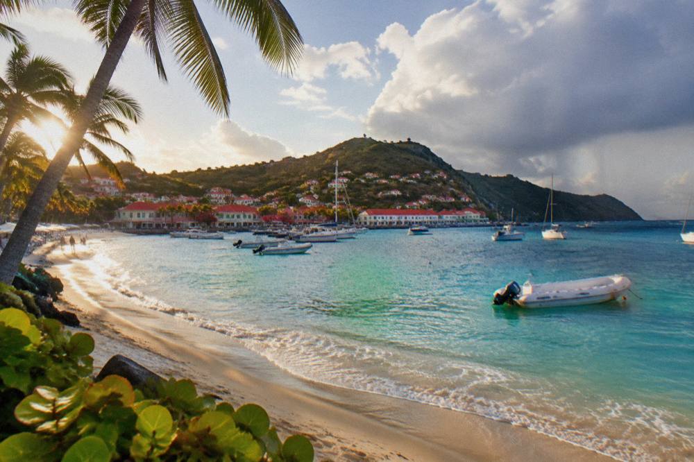 Sun low over a Caribbean beach on St Barts with palm trees leaning along the sand