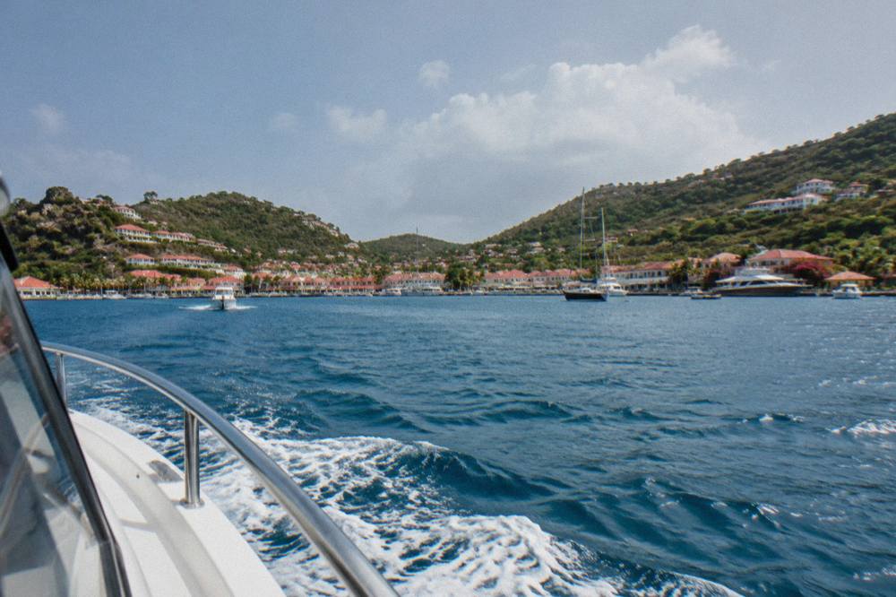 A private charter boat motoring across open blue water toward the green hills of St Barts
