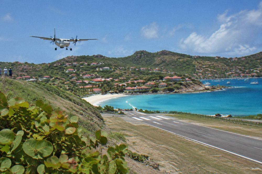 A small turboprop airplane on the short runway at Gustaf III Airport in St Barts with hills behind
