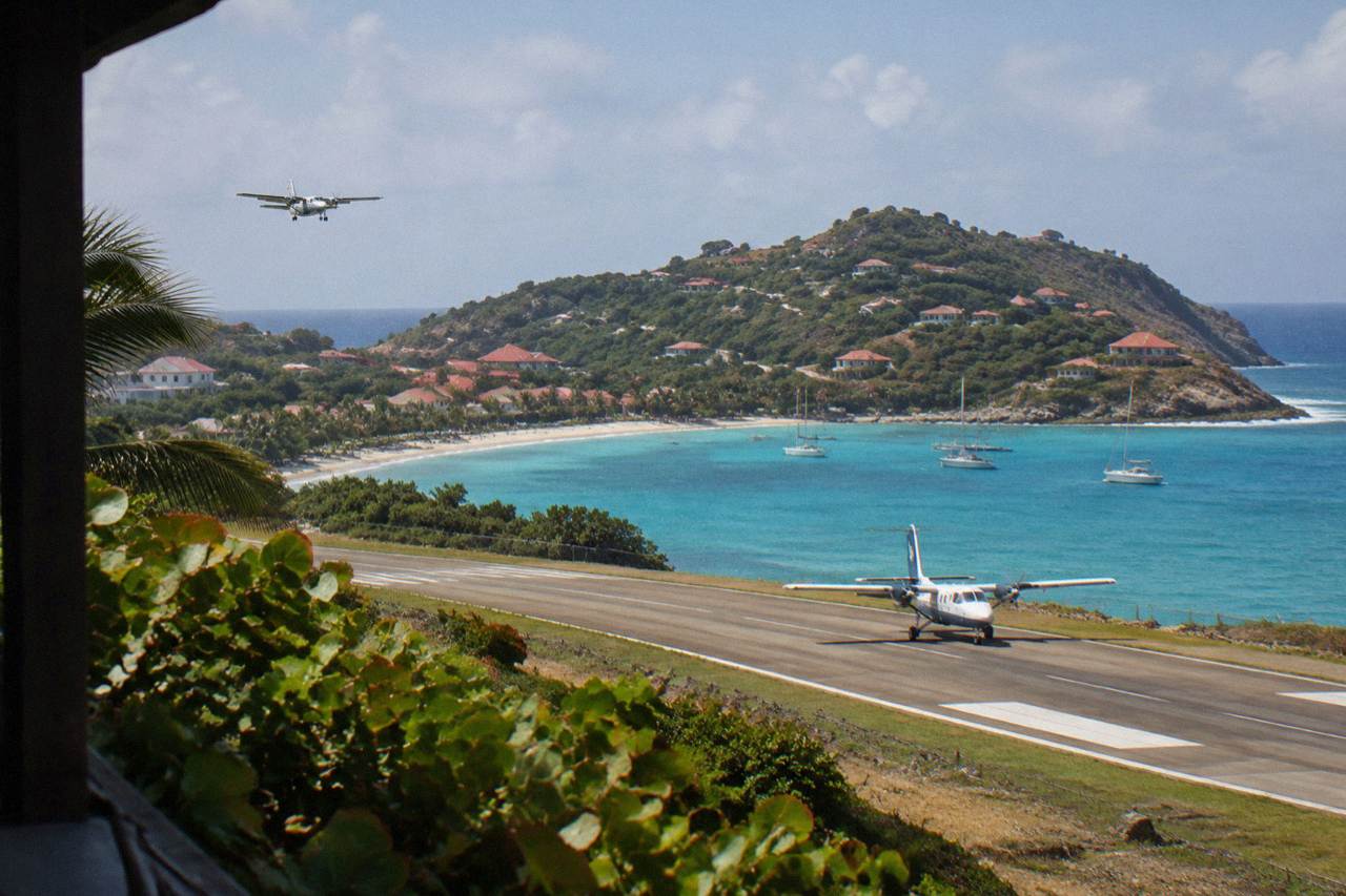 A small turboprop aircraft on the short runway at Gustaf III Airport in St Barts with green hills and turquoise water behind it