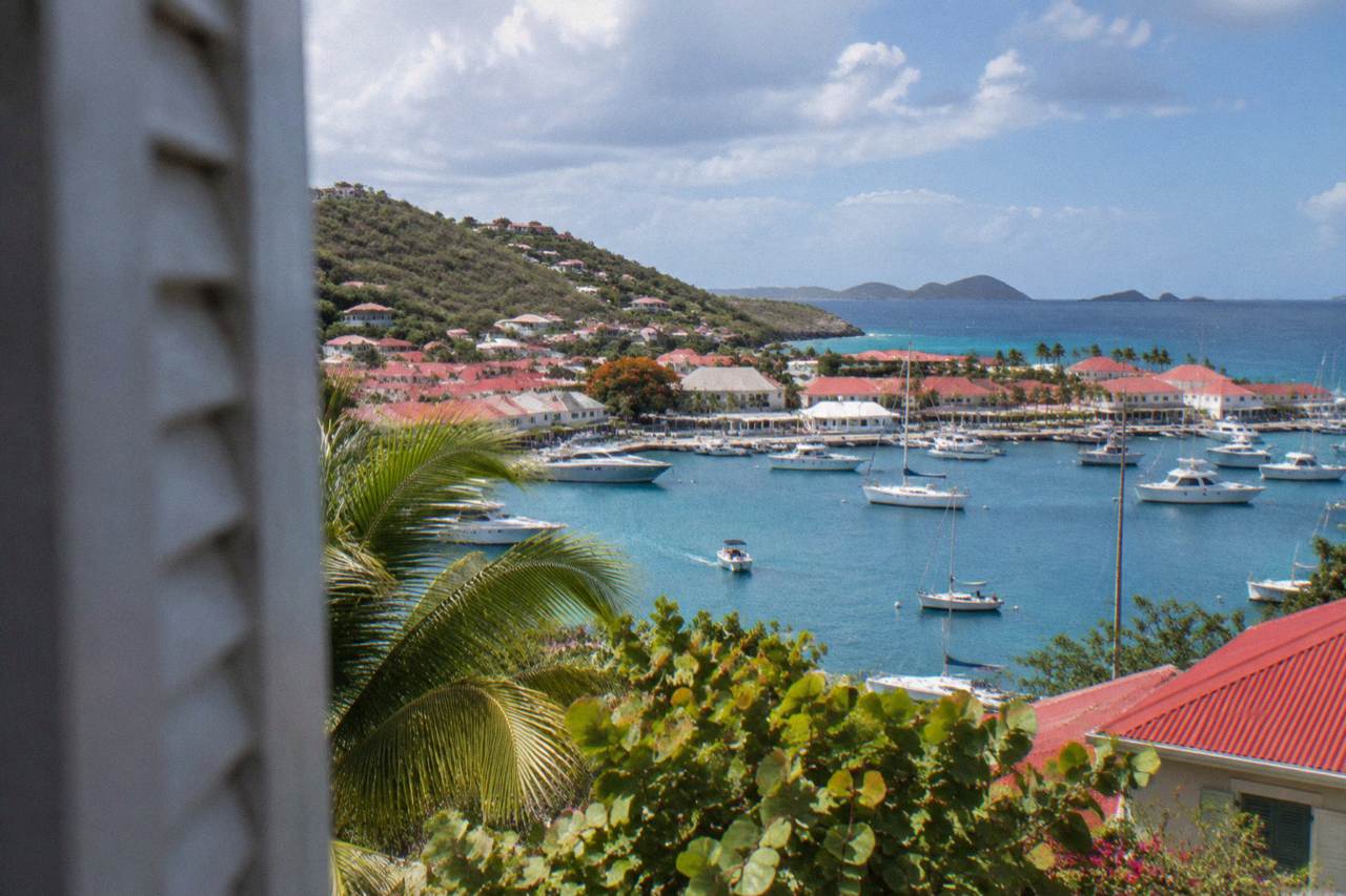 A green hillside on St Barts looking across turquoise Caribbean water toward distant islands on the horizon