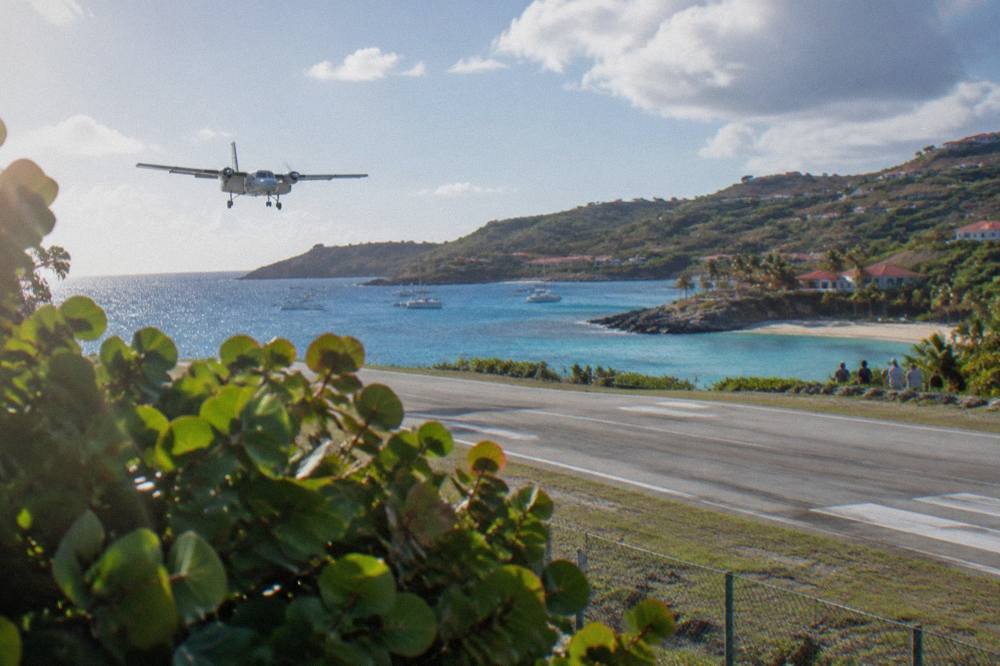 Small turboprop aircraft on the short runway at Gustaf III Airport in St Barts with hills and sea behind