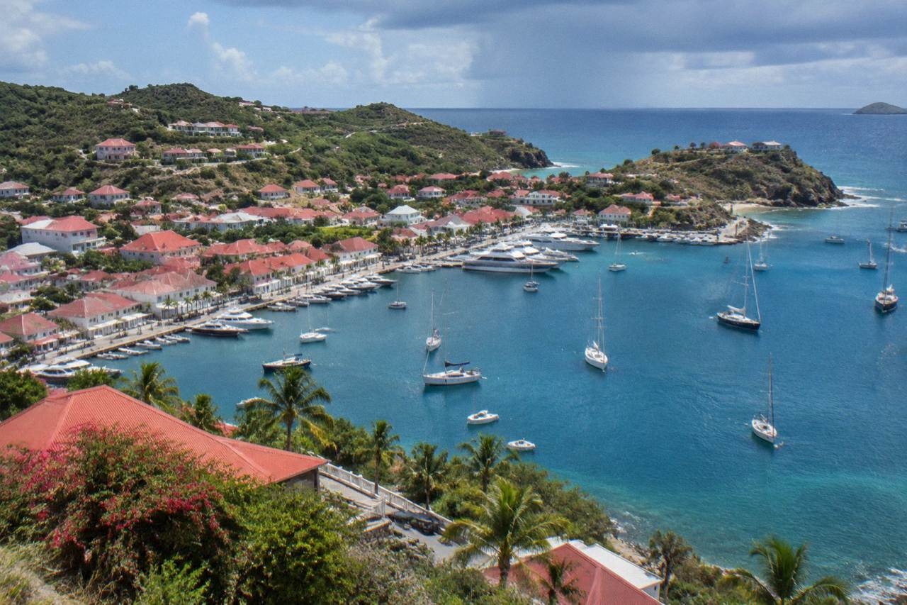 Aerial view of a green Caribbean island with turquoise water and sailboats anchored in a small harbor