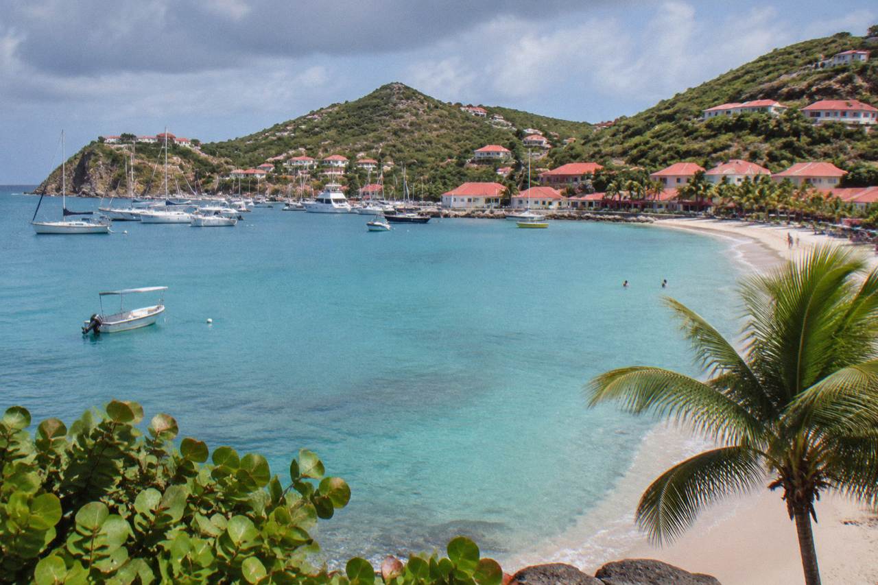 A curved Caribbean beach below green hills with calm turquoise water along the shoreline of St Barts