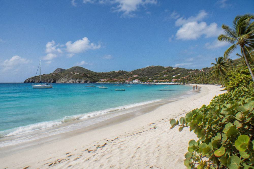 A wooded hillside trail looking down onto a small boat anchored in a quiet Caribbean bay