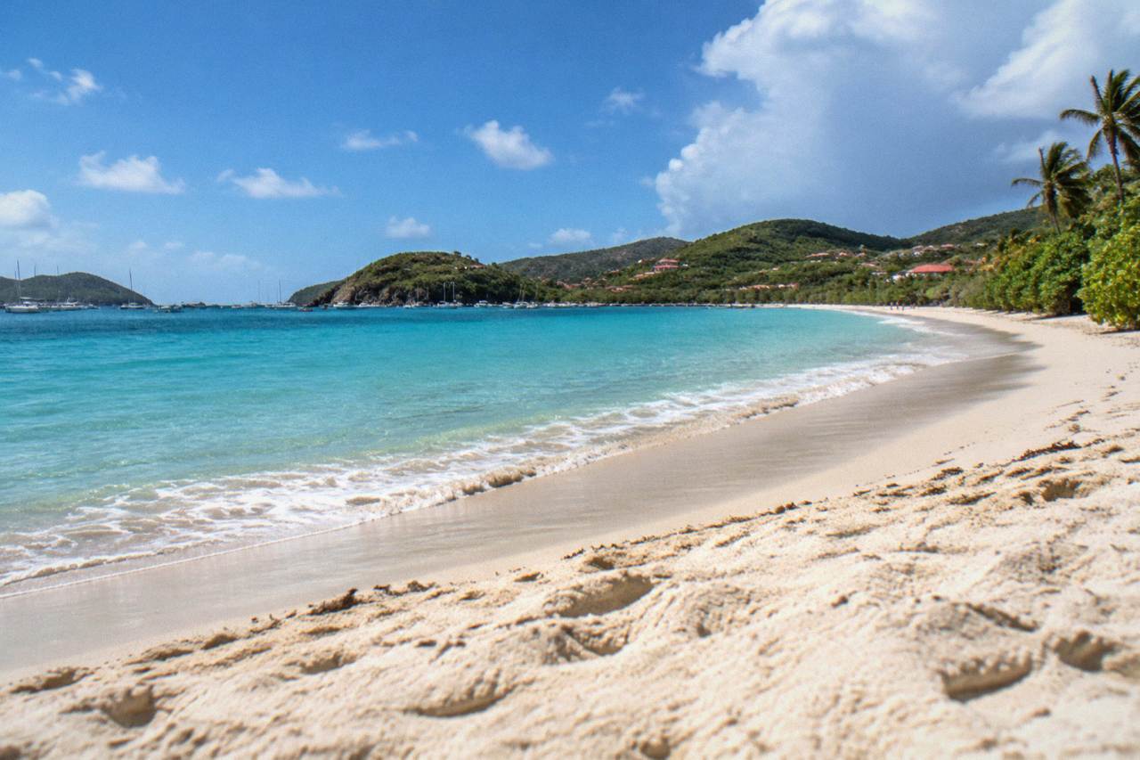 A curved sandy beach on a small Caribbean island with green hills rising behind it and clear turquoise water