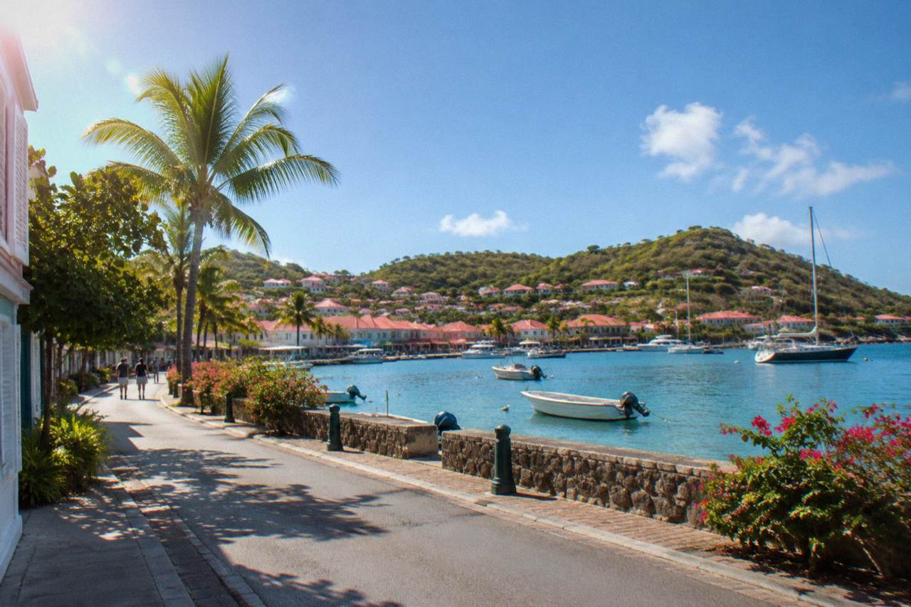 A sunny street in Gustavia with shop signs and a harbor view beyond