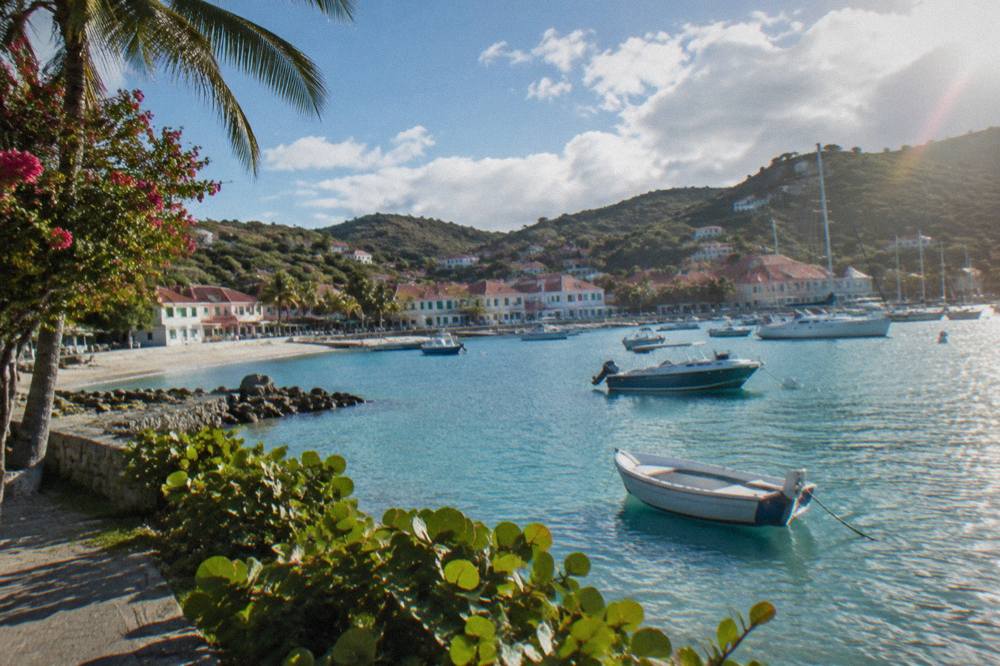A calm shallow lagoon with anchored small boats and a sandy beach curving around a bay