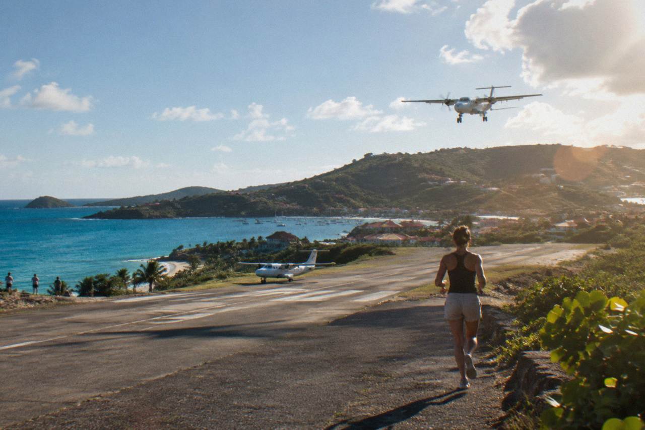 A small turboprop plane on the short runway at Gustaf III Airport in St Barts with hills behind it