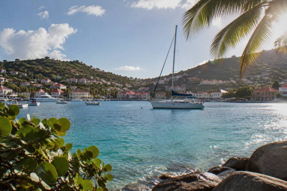 A sailboat anchored in clear water below green hills on the coast of St Barts