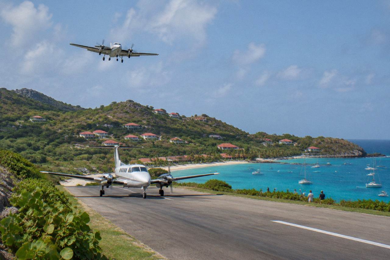 A small turboprop aircraft on the short runway at Gustaf III Airport in St Barts with green hills behind it