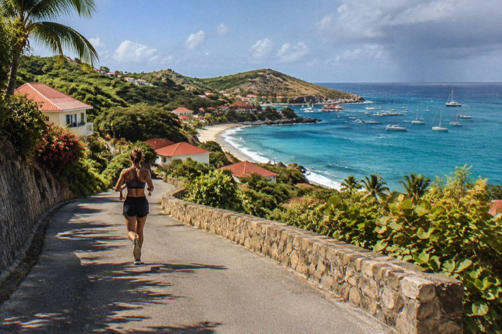 A narrow winding road with green hills climbing above a Caribbean bay