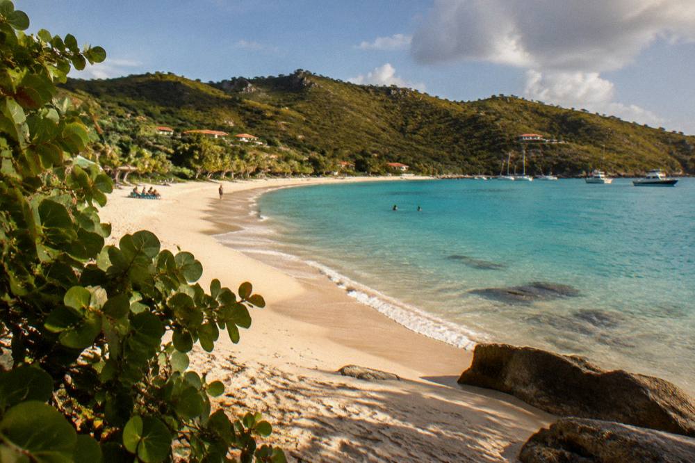The wide sandy curve of Gouverneur beach backed by green hills under a blue sky