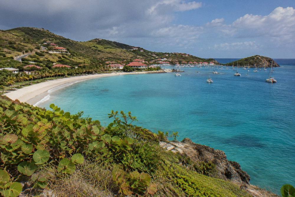 A curved sandy bay seen from a green headland with turquoise water beyond