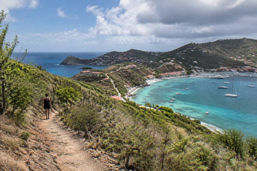 A steep dirt footpath winding through dry hillside scrub with a glimpse of sea below