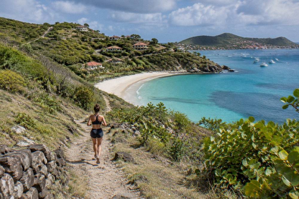 An empty crescent of sand backed by green hills and calm turquoise shallows