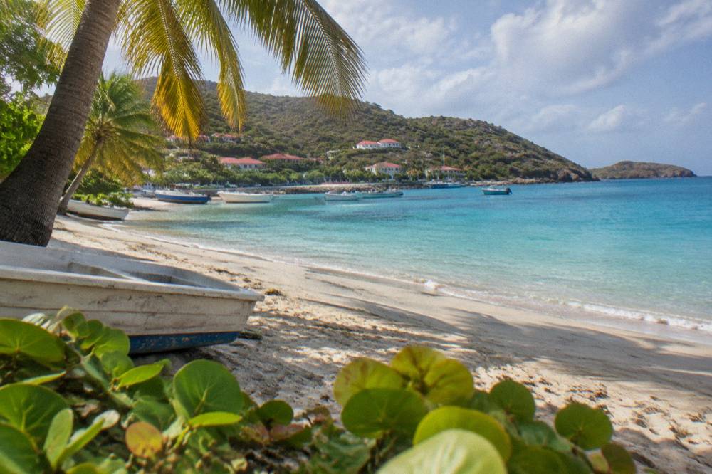 An empty Caribbean beach with soft sand, leaning palms and calm turquoise water