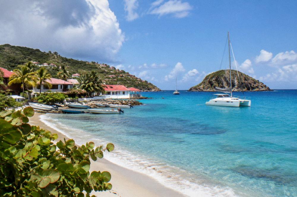 A sailing catamaran anchored in turquoise water near a rocky Caribbean islet