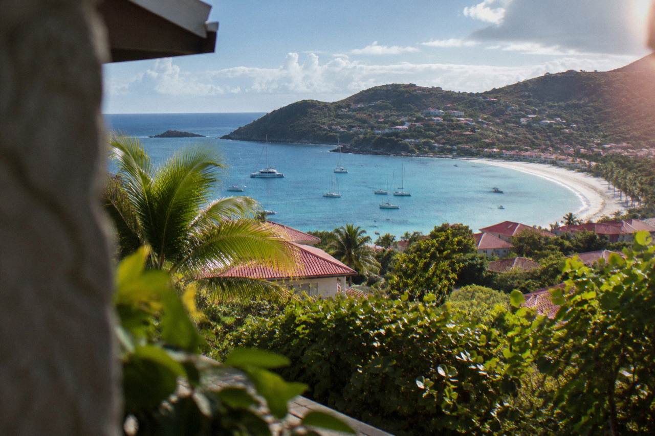 A hillside view over red rooftops toward a crescent beach and turquoise Caribbean water