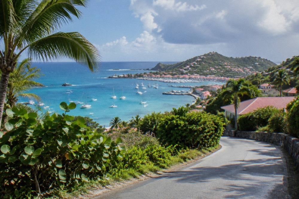 A narrow island road curving between green hills with sea in the distance