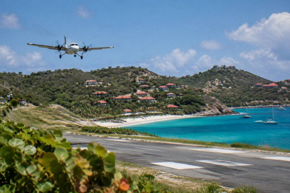 A small turboprop aircraft on a short runway beside a beach with hills behind