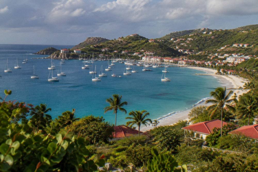 White sailboats moored in a harbour with hills and pastel buildings behind