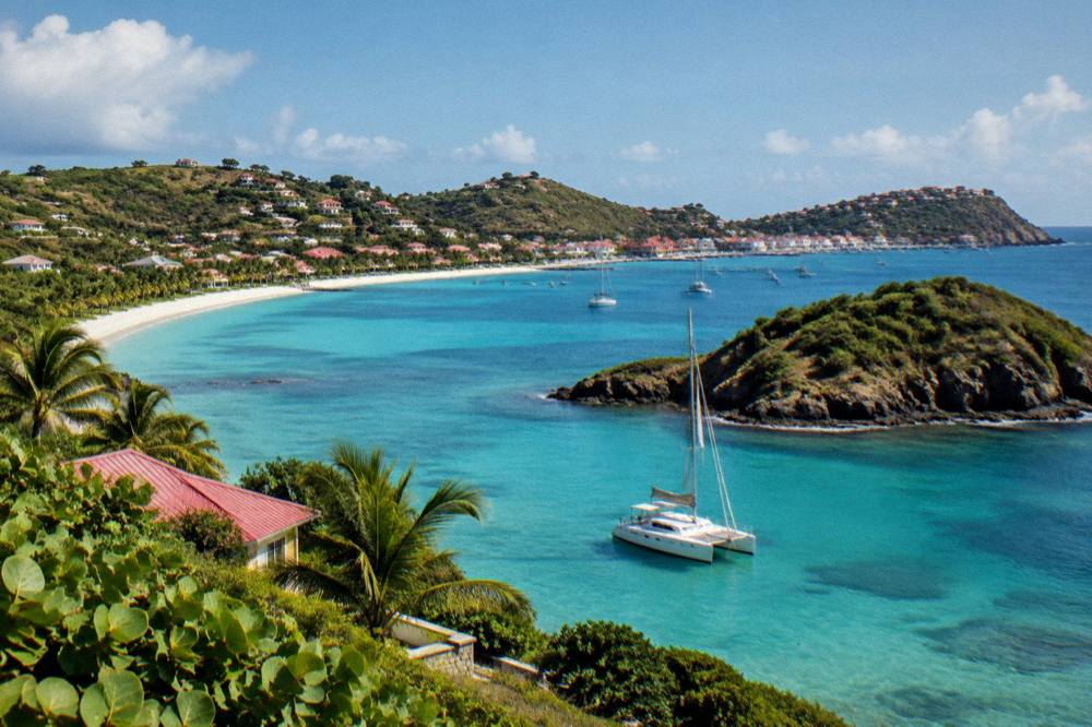 A catamaran anchored in clear shallow water beside a rocky green islet