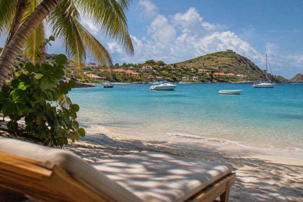 Wooden beach loungers under palms along a calm lagoon shore