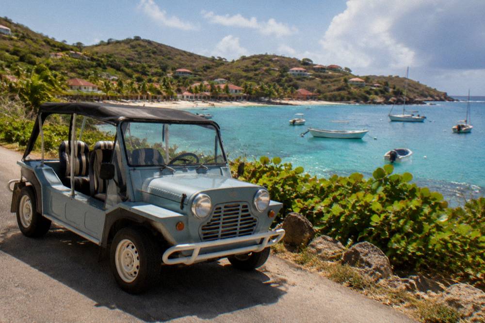 An open-top Mini Moke parked beside a narrow coastal road