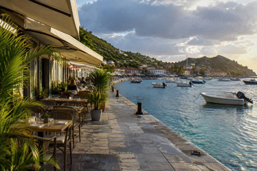 Evening light over a Caribbean harbour town with tables set along a stone quay