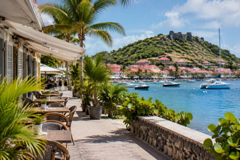 Stone fort ruins on a green hillside overlooking a harbour town and blue bay