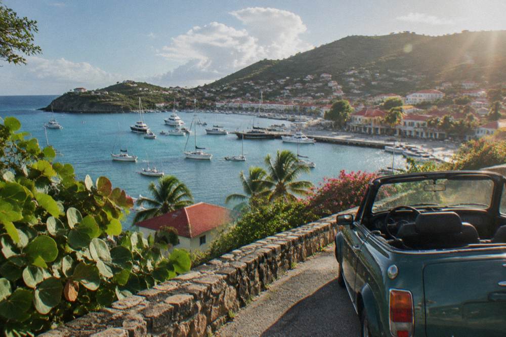 Small open-top car parked on a narrow hillside road above the sea